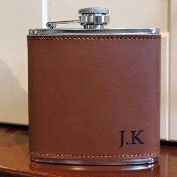 Een luxe roestvrijstalen Leren Heupfles met gegraveerd design, gepresenteerd in een zwarte geschenkdoos met een RVS trechter.