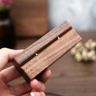 Zijaanzicht van een gesloten rechthoekig walnoot houten ringendoosje in een hand met focus op de natuurlijke houtnerf en afwerking.