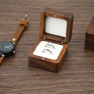 Geopend luxe walnoot houten ringdoosje met twee trouwringen in een wit fluwelen interieur, gepersonaliseerd met namen op de deksel.