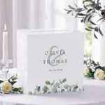 Witte acryl enveloppendoos met eucalyptus design in saliegroene tinten op receptietafel met witte rozen, gepersonaliseerd met namen en datum