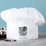 Witte koksmuts bedrukt met "I Cook as Good as I Look" en gepersonaliseerd met "(Naam's) Keuken"