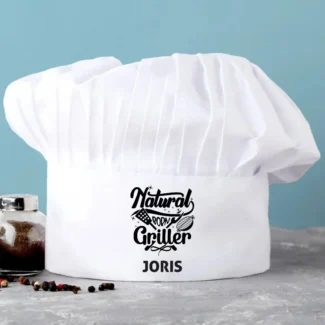 Witte gepersonaliseerde koksmuts met de tekst "Naturel Born Griller" en een naam