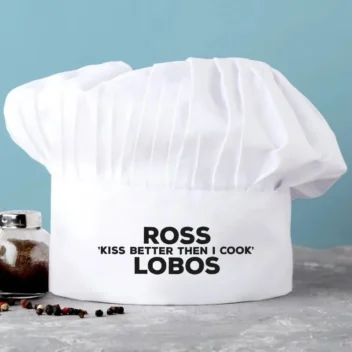 Witte koksmuts bedrukt met "Kiss Better Than I Cook" en gepersonaliseerd met naam