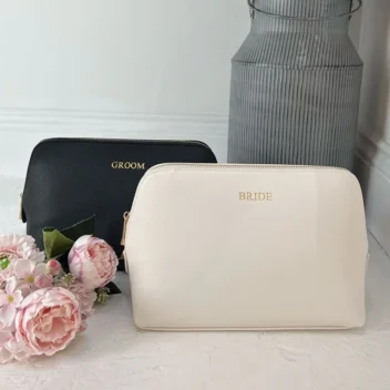 Set van twee luxe toilettassen van kunstleer: een oesterwitte tas met gouden 'Bride'-opdruk en een zwarte tas met gouden 'Groom'-opdruk – perfect als huwelijks- of vrijgezellencadeau