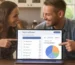 Een ontspannen stel zit aan de keukentafel en plant hun bruiloft met de online wedding planner tool op een laptop, waarbij ze de afvinklijst en het budget beheren.