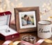 Een feestelijke banner met gepersonaliseerde cadeaus, zoals een gegraveerde juwelendoos, een fotolijst met familie foto en een mok met naam, op een zachte pastelachtergrond met linten en confetti.