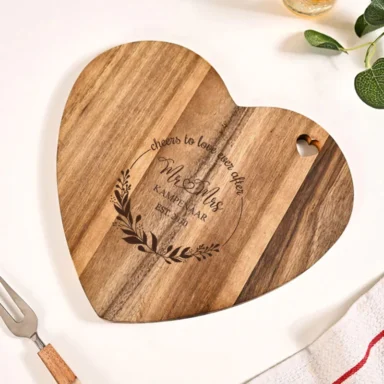 Gepersonaliseerde hartvormige snijplank van acaciahout, gegraveerd met een 'Mr & Mrs' krans, achternaam en jaartal, met een decoratieve hartvormige uitsnijding.