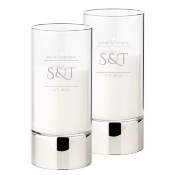 Set van twee zilverkleurige windlichten met wit-matte glasgravure 'S&T EST. 2026' in een modern minimalistisch design.