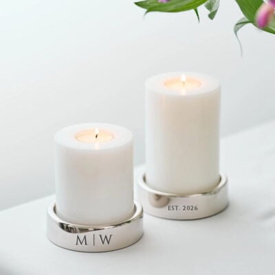 Set van twee luxe vernikkelde zilveren kaarshouders, asymmetrisch gegraveerd met initialen en een tekstregel op een fluwelen voet.