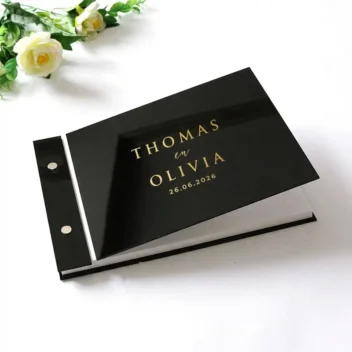 Hoogglans zwart acryl gastenboek met goud spiegel monogram, liggend op een marmeren tafel