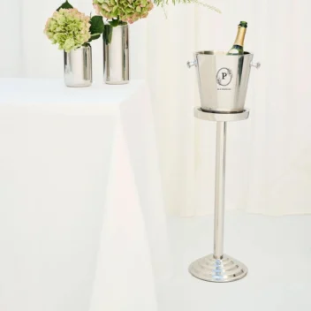 Luxe RVS wijnkoeler op hoge standaard in een stijlvol interieur met bloemen en witte tafel.