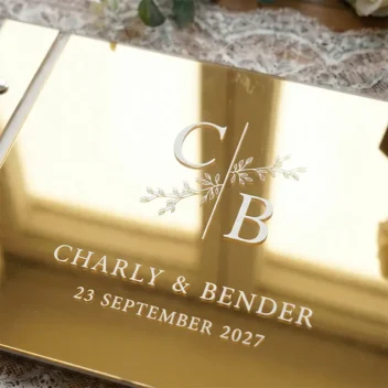 Detail bedrukking gastenboek mirror acryl botanisch monogram goud met witte UV print initialen takje namen en datum