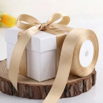 Rol champagne satijn lint naast een gestrikte witte cadeaubox op een houten ondergrond