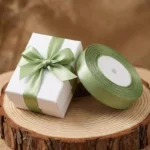 Rol luxe olijfgroen satijn lint van 1,5 cm breed naast een gestrikt wit cadeaudoosje voor een botanische bruiloft.