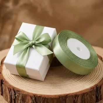 Rol luxe olijfgroen satijn lint van 1,5 cm breed naast een gestrikt wit cadeaudoosje voor een botanische bruiloft.