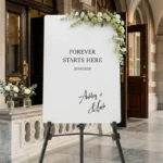 Ashley Script Welkomstbord in wit acryl met vaste tekst Forever Starts Here en namen Ashley en Chris in handgeschreven script op schildersezel bij kerkentree
