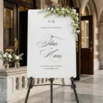 Florence Monogram Welkomstbord in wit acryl met zwarte scripttypografie, monogram initialen en namen op schildersezel bij stadhuisentree