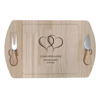 Houten borrelplank met gravure van twee verstrengelde harten en tekst "25 jaar liefde & geluk – De familie Jansen", met twee magnetische messen aan de zijkant