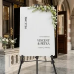 Vincent Modern Welkomstbord in wit acryl met zwarte kapitalen, verticale WELCOME tekst en namen Vincent en Petra op schildersezel bij stadhuis entree